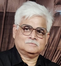 Portrait of an older man with white hair and glasses, wearing a black shirt, looking at the camera.