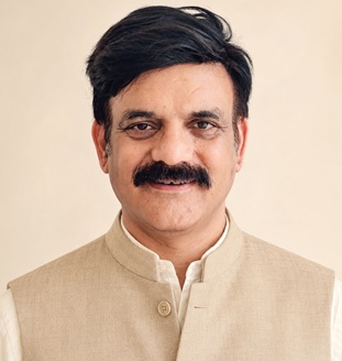 Portrait of a middle-aged man with dark hair and a mustache, wearing a beige Nehru jacket against a light background.