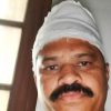 Close-up of a man with a white head wrap/bandage and a mustache, looking at the camera indoors.