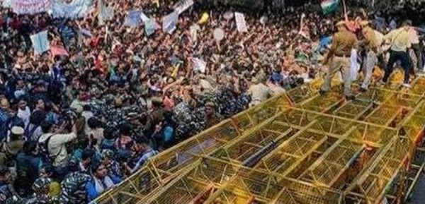Dense crowd of protesters surrounding a yellow metal scaffold-like platform on a vehicle, in a chaotic public demonstration scene.