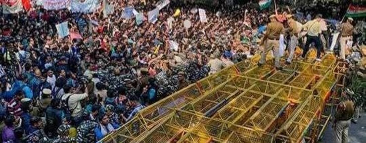 Dense crowd of protesters surrounding a yellow metal scaffold-like platform on a vehicle, in a chaotic public demonstration scene.