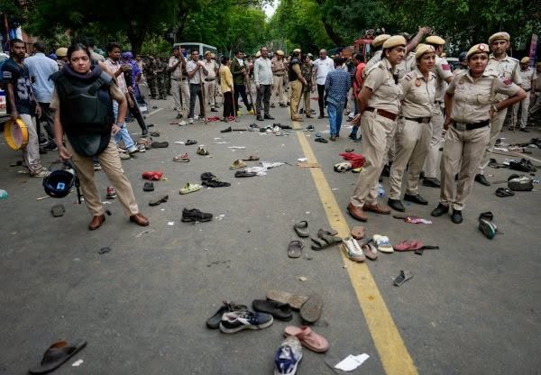 protest_1 | No. 1 Indian Media News Portal Uniformed police stand on a road with numerous scattered shoes and belongings along the center line, civilians in the background.
