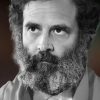 Close-up portrait of a bearded man with a thick gray beard and contemplative expression.