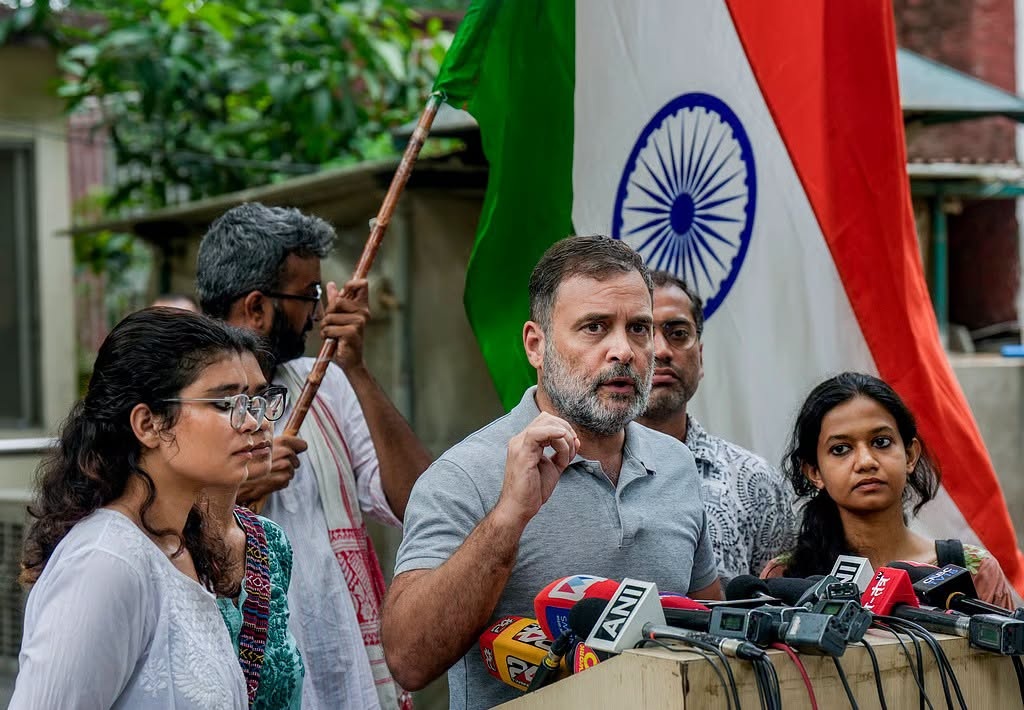 rahul_1 | No. 1 Indian Media News Portal Man with gray beard addresses a crowd at a press conference, microphones in front, Indian flag in the background.