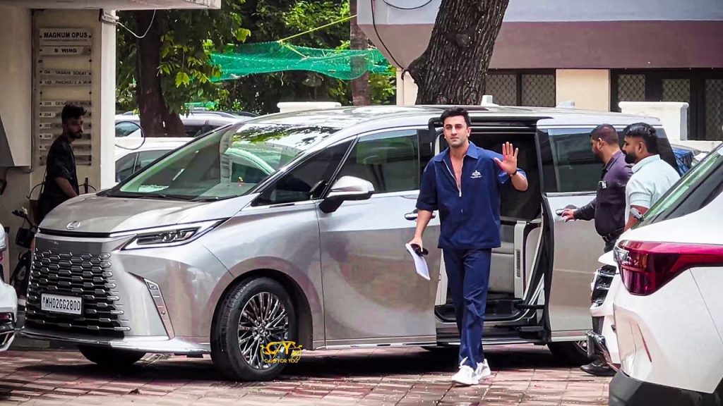 ranveer | No. 1 Indian Media News Portal Man in a blue tracksuit waves while stepping out of a silver minivan, holding papers; two men stand nearby.