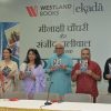 Six people standing behind a table at a book launch, each holding a copy of the same book with a blue cover.