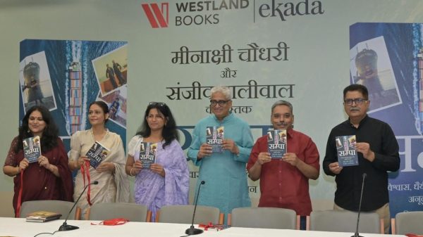 Six people standing behind a table at a book launch, each holding a copy of the same book with a blue cover.