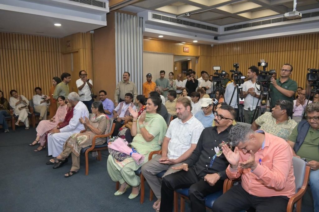 relese_1 | No. 1 Indian Media News Portal Audience seated in a conference room, some clapping, with photographers and video cameras visible at the back of the room.