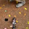 Broadcast microphone lying on wet pavement among yellow leaves, with a shoe visible in the background.