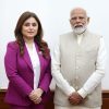 Woman in a magenta suit standing beside a man in a beige traditional-style vest, both in formal attire against a plain background.