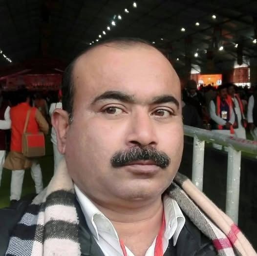 Close-up of a man with a mustache wearing a black-and-white scarf at a crowded indoor event.