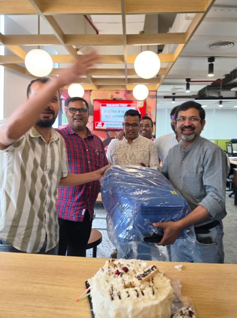 sanjay srivastav | No. 1 Indian Media News Portal Group of coworkers celebrating in an open office, posing with a large blue wrapped item while a cake sits on the table in front.