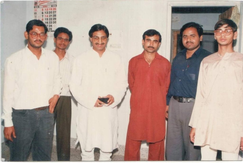 sanjay_dixit | No. 1 Indian Media News Portal Six men stand side by side indoors, facing the camera. From left: a man in a white shirt and dark trousers; a man in a light striped shirt; a man in a white kurta; a man in a red kurta; a man in a dark blue shirt and gray trousers; and a man in a light kurta with glasses.