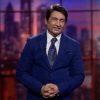 Male host in a blue suit on the Shekhar Tonight TV set, smiling with hands clasped in front of a cityscape backdrop.