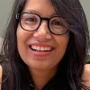 Close-up portrait of a smiling woman with shoulder-length dark hair and black-framed glasses facing the camera.