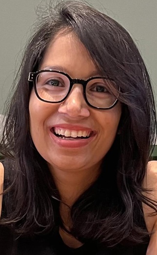 Close-up portrait of a smiling woman with shoulder-length dark hair and black-framed glasses facing the camera.