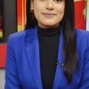 Professional woman in a royal blue blazer seated at a news desk, facing the camera.