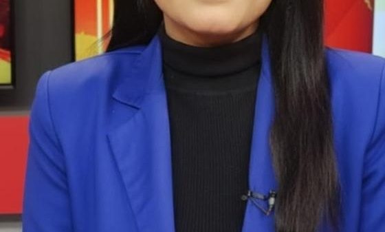 Professional woman in a royal blue blazer seated at a news desk, facing the camera.