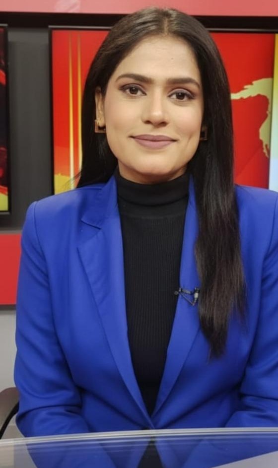 Professional woman in a royal blue blazer seated at a news desk, facing the camera.