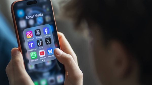 Person holding a smartphone displaying a folder of social media app icons (Instagram, Facebook, TikTok, YouTube).