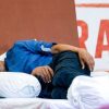 Man sleeping on a white pillow on a bed, wearing a blue shirt, with flowers in the foreground and red lettering in the background.