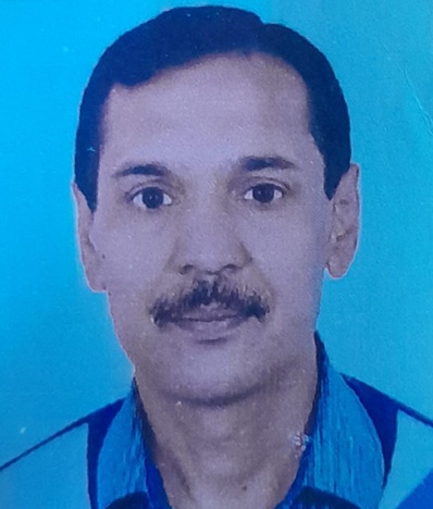 Portrait of a man with short dark hair and mustache wearing a blue shirt against a blue background.