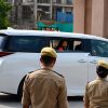 Bearded man in a white van waves from the window while security personnel in khaki uniforms stand nearby.
