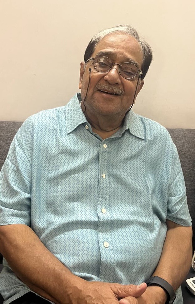 04b917d2-727f-4c90-96db-8eac983b2ada | No. 1 Indian Media News Portal Smiling elderly man with glasses sitting on a sofa, wearing a light blue patterned shirt.