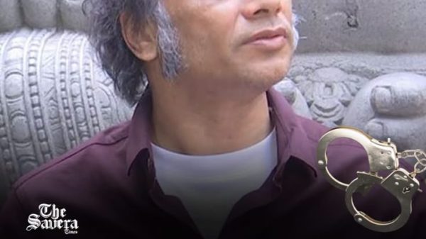 News post image: man in a maroon shirt with a carved stone background and a handcuffs graphic, about Vijay Aggarwal detention.