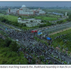 Aerial view of a large crowd marching along a road toward the Jharkhand Assembly in Ranchi, with the building visible in the distance.