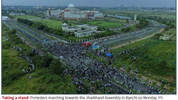 Aerial view of a large crowd marching along a road toward the Jharkhand Assembly in Ranchi, with the building visible in the distance.