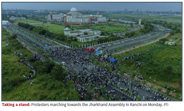 Aerial view of a large crowd marching along a road toward the Jharkhand Assembly in Ranchi, with the building visible in the distance.
