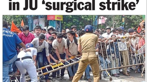 Crowd of protesters pushes against metal barricades as a police officer in khaki maintains a line, during a confrontation near Jadavpur University.