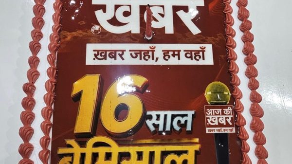 Celebration cake with red frosting and Hindi text announcing 16 years of Aaj Ki Khabar news channel, with a small microphone graphic.