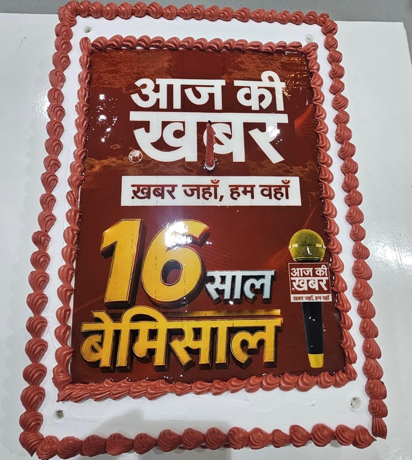 Celebration cake with red frosting and Hindi text announcing 16 years of Aaj Ki Khabar news channel, with a small microphone graphic.
