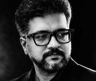 Portrait of a man with glasses and a beard, looking to the right, wearing a dark shirt in a studio setting.