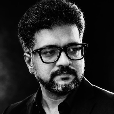 Portrait of a man with glasses and a beard, looking to the right, wearing a dark shirt in a studio setting.
