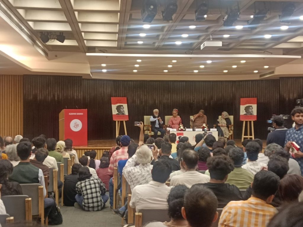 arundhati | No. 1 Indian Media News Portal Panel discussion in a large auditorium with five speakers on stage and a seated audience watching attentively.