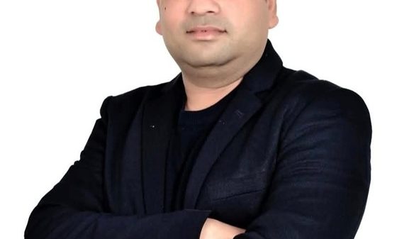 Professional portrait of a man in a dark blazer with arms crossed against a white background.