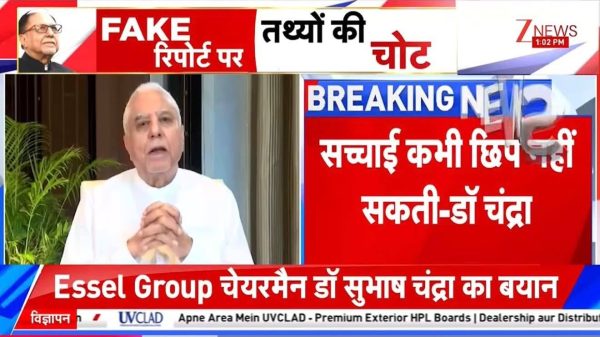 TV news screenshot showing a man in a white kurta speaking, with bold red and blue breaking-news banners and Hindi text overlays. Bottom ticker reads 'Essel Group...' in white on red.