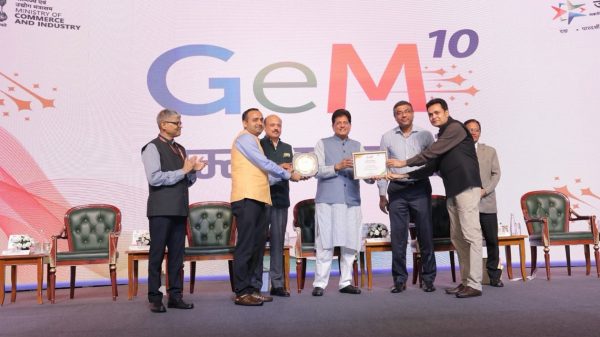 Group of men on stage during GeM 10 awards ceremony, exchanging a plaque with a backdrop displaying GeM 10 and ministry logos.
