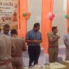 Group of police officers and civilians chatting under orange drapes at a Bhoomi Pujan ceremony with a Hindi banner in the background.