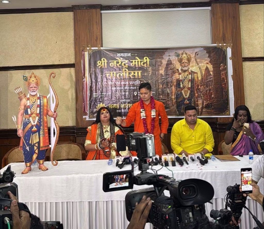 img_0580 | No. 1 Indian Media News Portal Press conference scene with a large Hindu deity banner and a life-size cutout, people seated at a table with microphones and cameras filming.