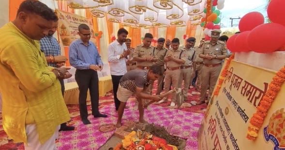 Group of men, including police officers, standing around a ritual fire and offerings at a decorative ceremony outdoors with orange decorations and garlands.