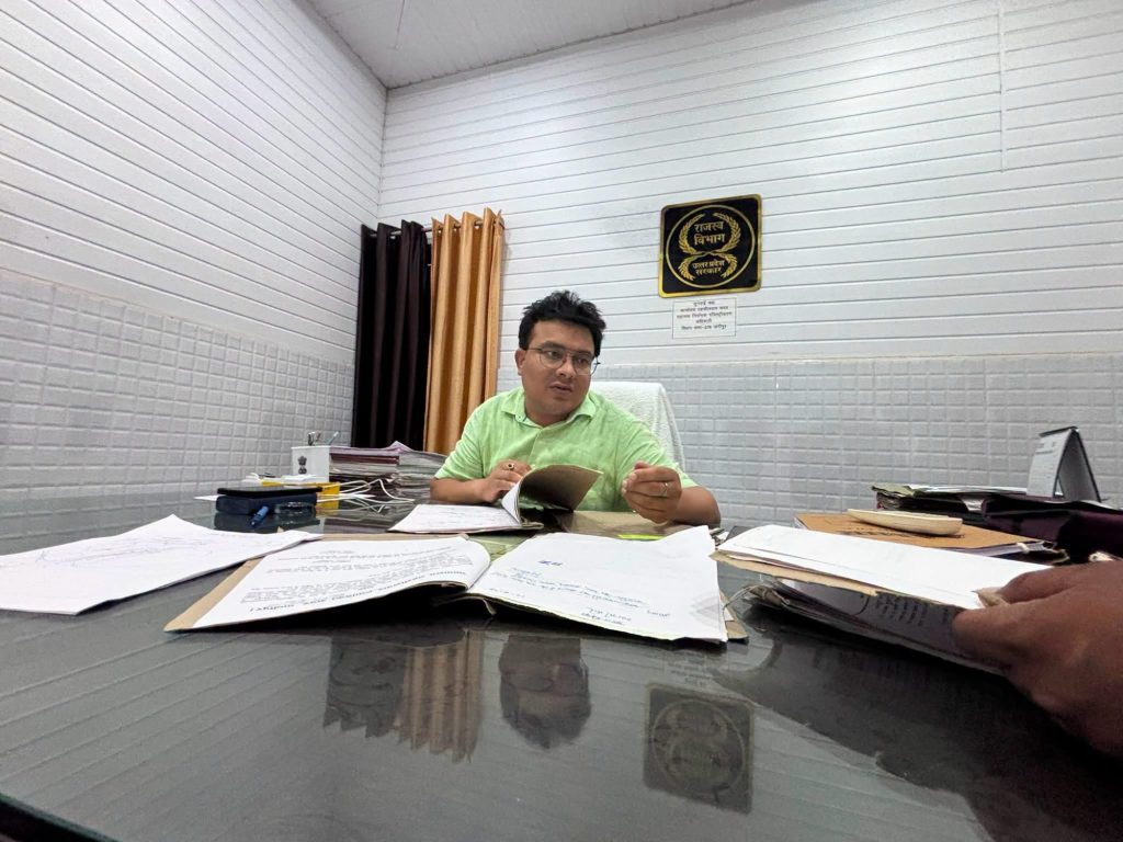 img_0804 | No. 1 Indian Media News Portal Man in a light-green shirt sits at a cluttered desk, reviewing a folder amid scattered papers in a white-paneled office.