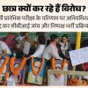Students protest at a rally with garlanded framed portraits laid on a table and supporters holding Hindi protest signs in the background.
