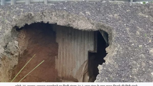 Roadway collapse visible: large hole in asphalt with exposed soil and a concrete wall beneath the road near a guardrail, suggesting a sinkhole.