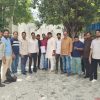 Group of men standing in a line outside on a paved courtyard under trees, posing for a photo.