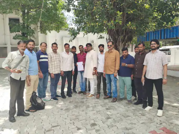 Group of men standing in a line outside on a paved courtyard under trees, posing for a photo.
