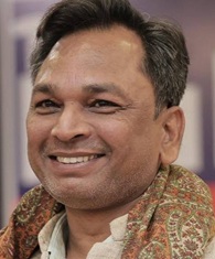 Smiling man with short dark hair wearing a patterned scarf, looking at the camera.